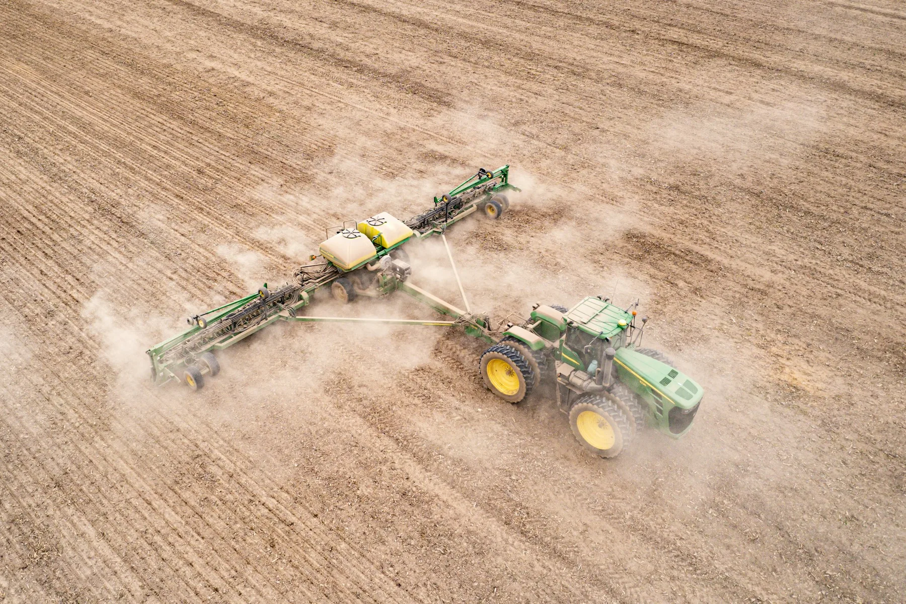 A tractor-mounted boom sprayer working across a field